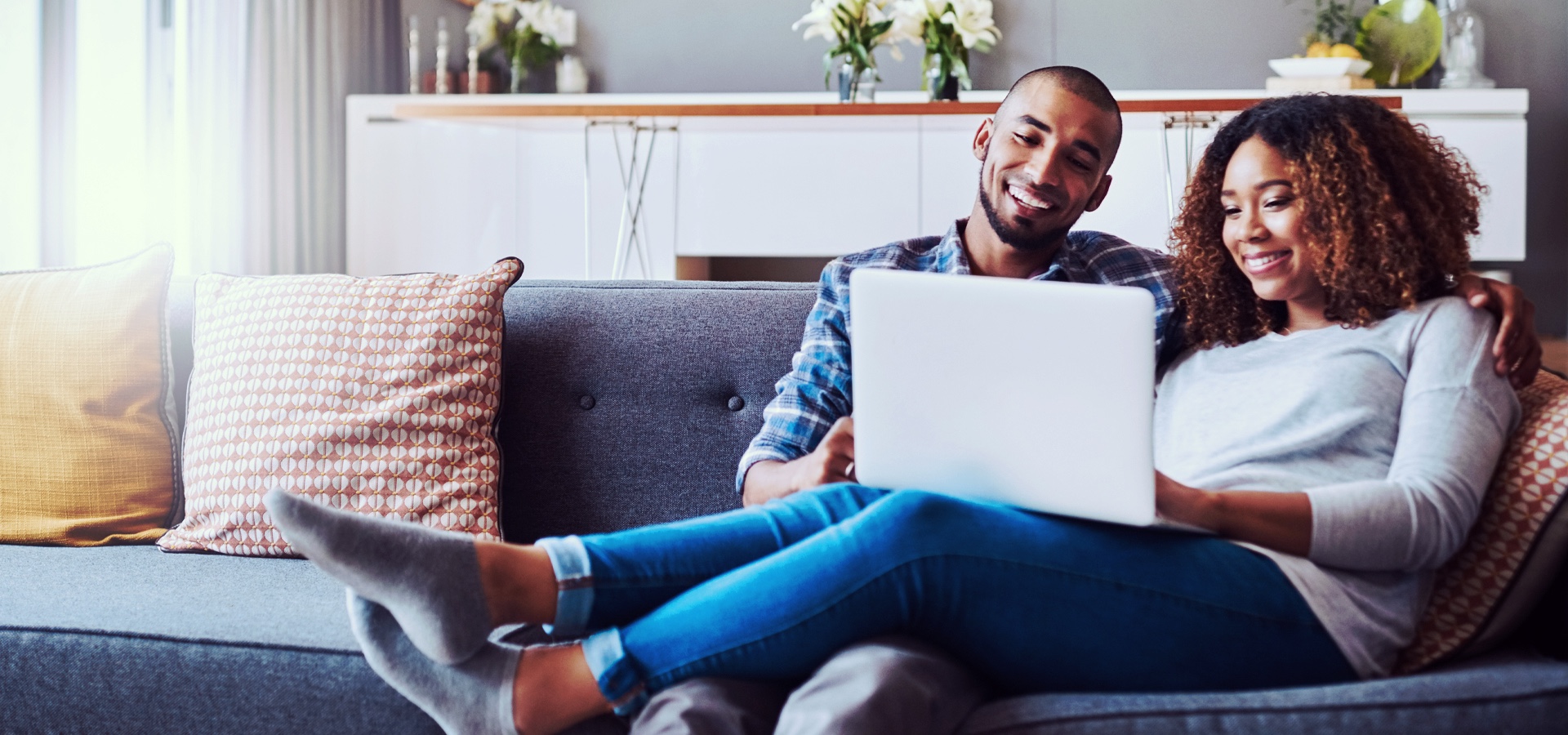 couple sitting on a couch smiling at the laptop in woman's hands