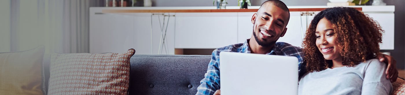 couple sitting on a couch smiling at the laptop in woman's hands