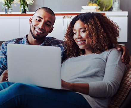couple sitting on a couch smiling at the laptop in woman's hands